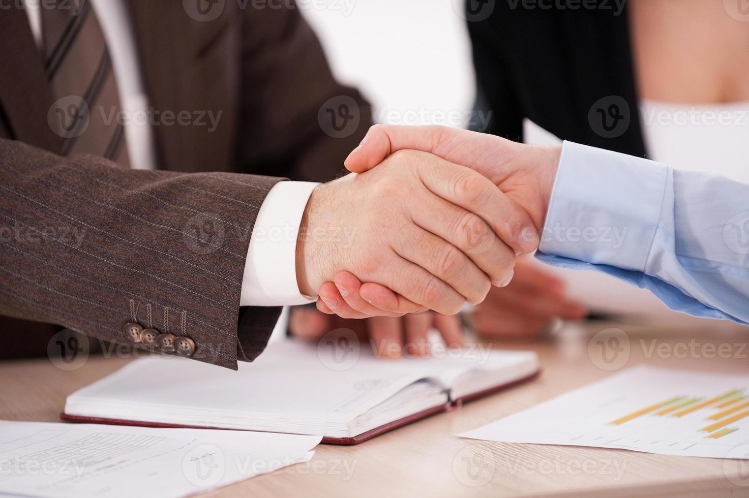 tätning en handla. närbild av två företag män skakning händer medan Sammanträde på de tabell foto