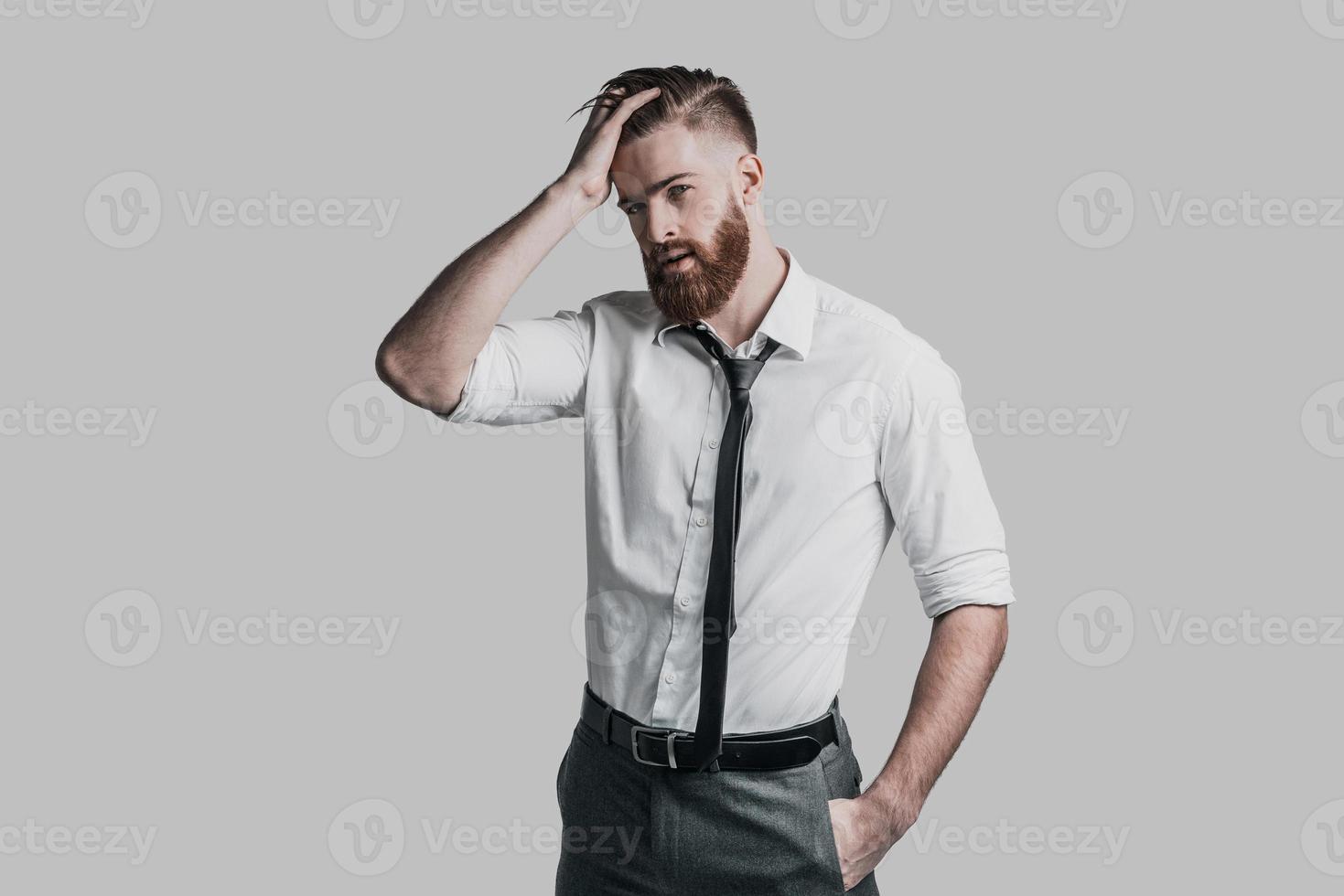 vit krage stilig. stilig affärsman innehav hand på huvud och ser på kamera medan stående mot grå bakgrund foto