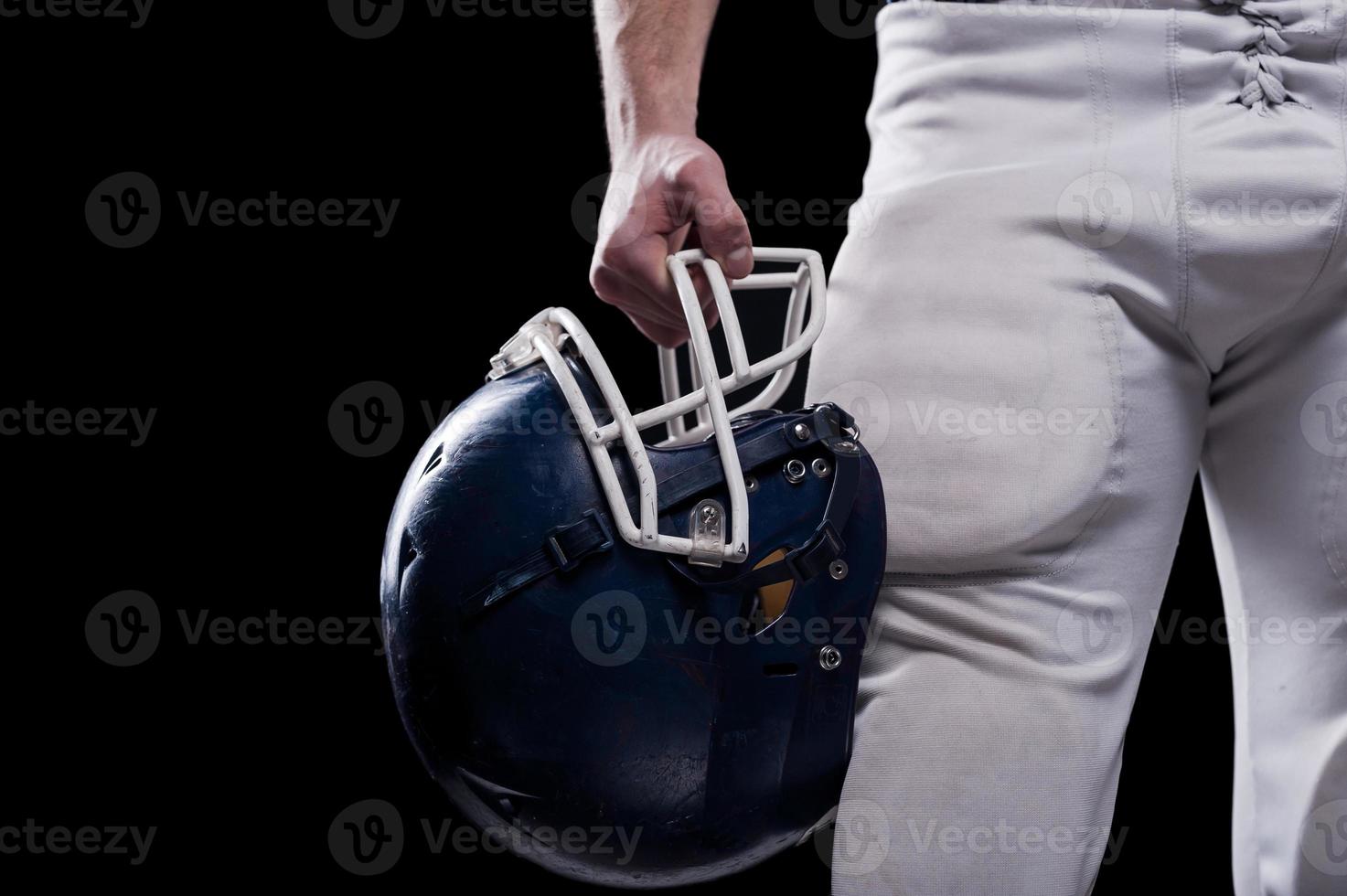 krascha hjälm. beskurna bild av amerikan fotboll spelare innehav fotboll hjälm medan stående mot svart bakgrund foto