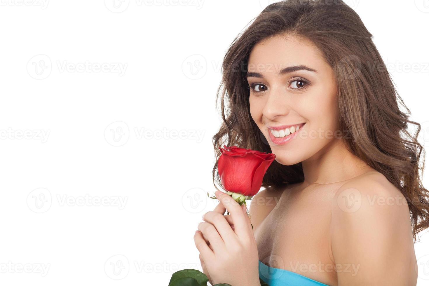 skönhet med blomma. attraktiv ung kvinna innehav en röd reste sig och leende på kamera medan stående isolerat på vit bakgrund foto
