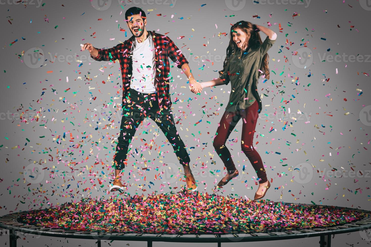 bara för roligt. i luften skott av skön ung glad par innehav händer medan Hoppar på trampolin tillsammans med konfetti Allt runt om dem foto