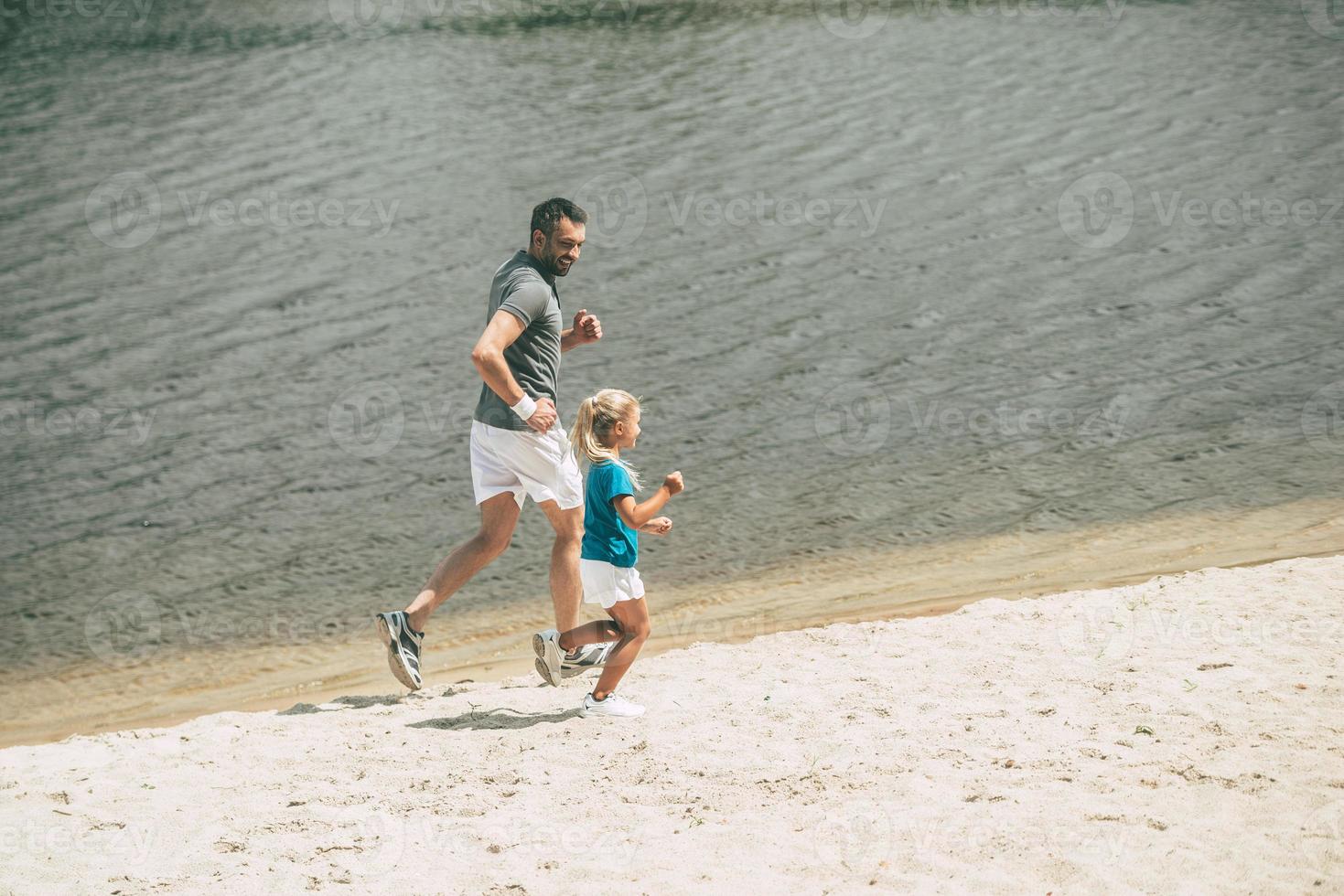 njuter joggning på färsk luft. topp se av glad far och dotter i sporter kläder joggning på de flodbank tillsammans foto