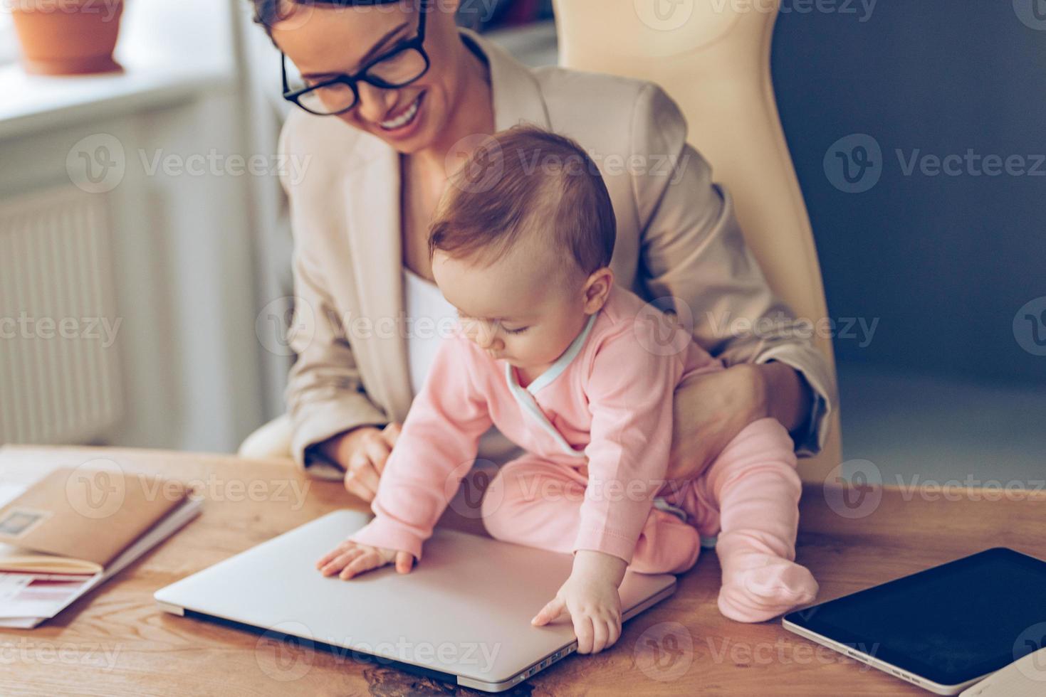 sluta arbetssätt liten bebis flicka stängning bärbar dator medan Sammanträde på kontor skrivbord med henne mor i kontor foto