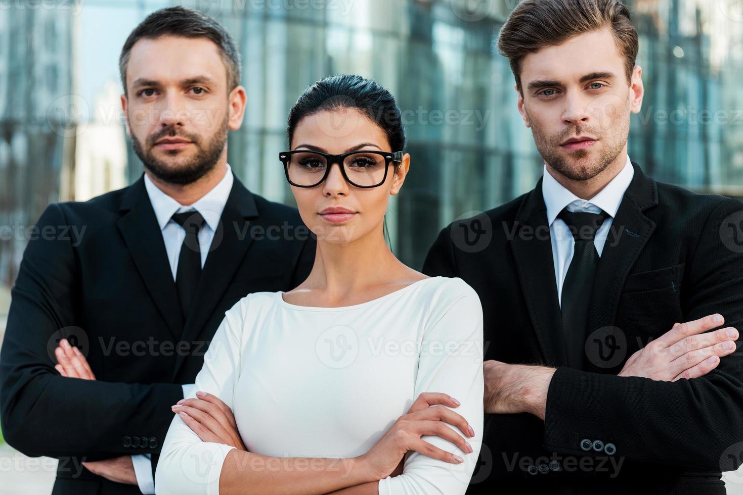 ansikten av ny företag. tre självsäker företag människor förvaring vapen korsade och ser på kamera medan stående utomhus foto
