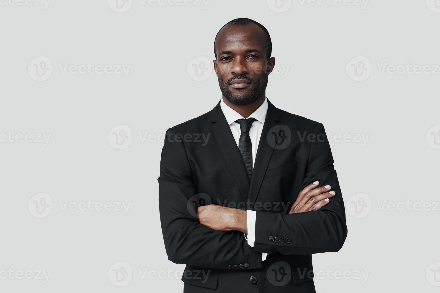 stilig ung afrikansk man i formell klädsel ser på kamera medan stående mot grå bakgrund foto