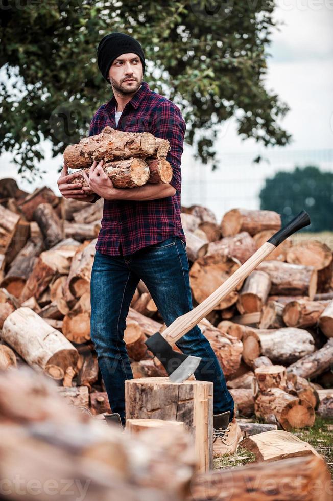 skogsarbetare på arbete. stilig ung skogvaktare innehav loggar och ser bort medan stående utomhus foto