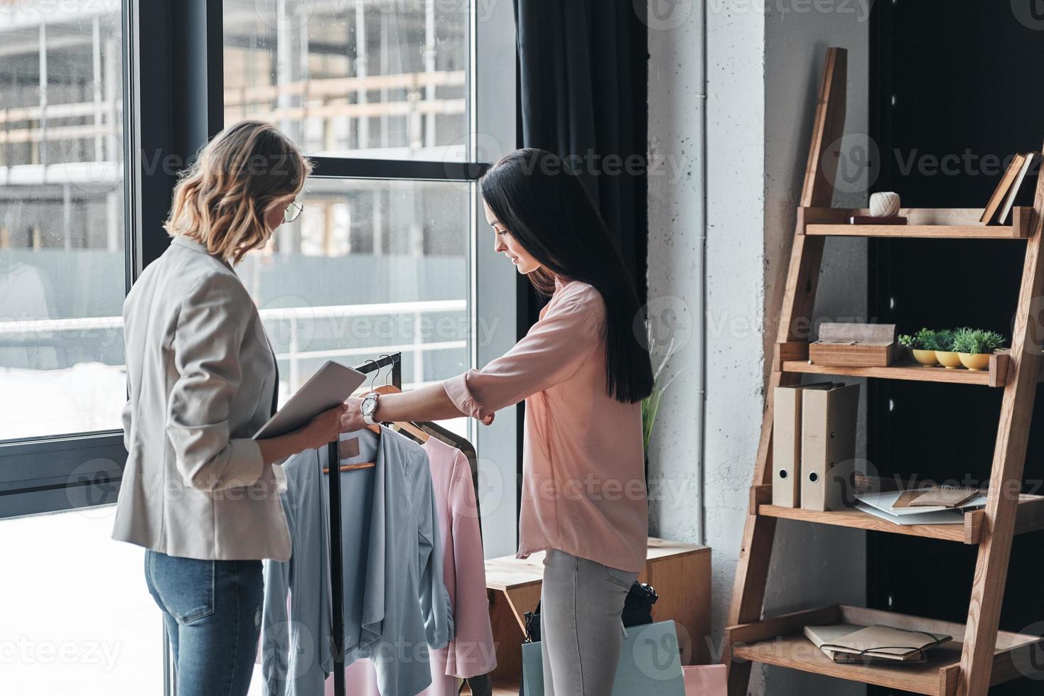 vänlig service. skön ung kvinna portion till välja kläder till henne kund medan arbetssätt i de mode boutique foto