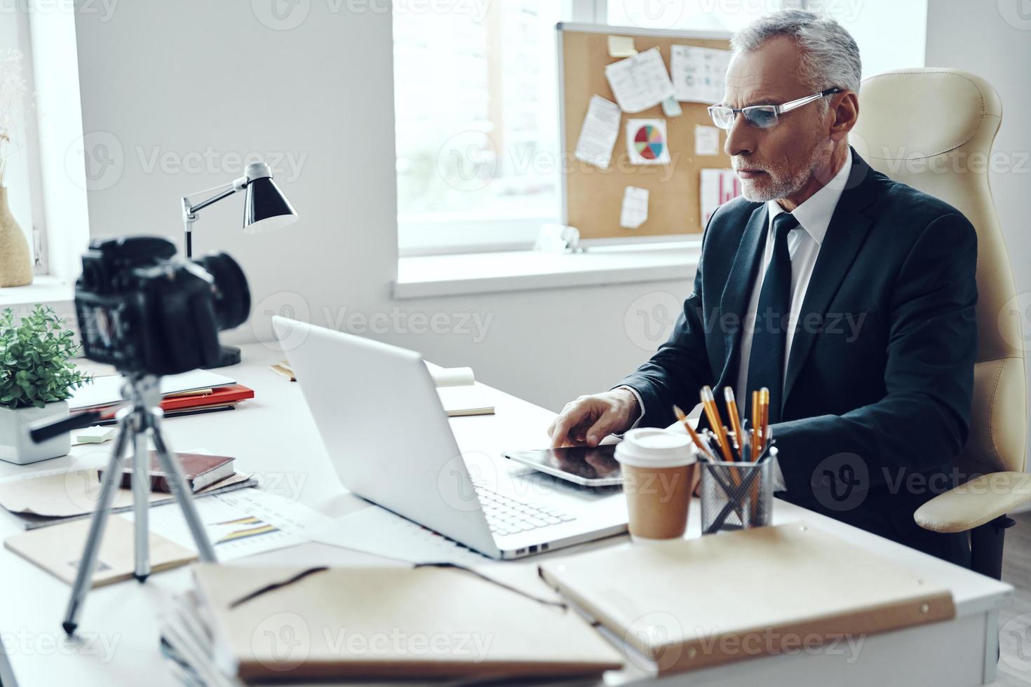 senior man i elegant företag kostym använder sig av modern teknik medan framställning social media video foto
