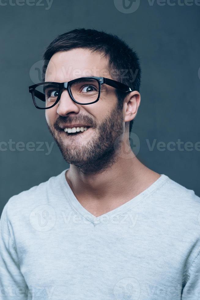 tycka om en nörd. ung nörd man i glasögon framställning en ansikte medan stående mot grå bakgrund foto