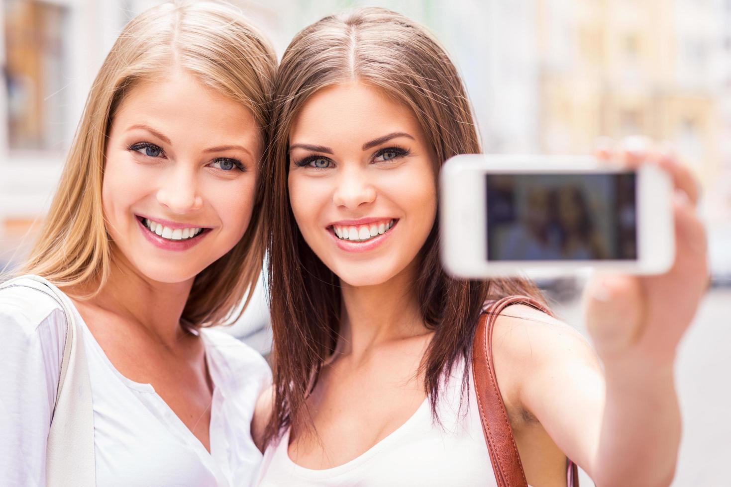 kvinnor framställning selfie. två attraktiv ung kvinnor framställning selfie och leende medan stående utomhus foto