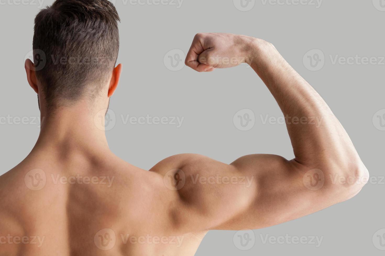 som visar hans perfekt biceps. bak- se av ung muskulös man som visar hans biceps medan stående isolerat på grå bakgrund foto