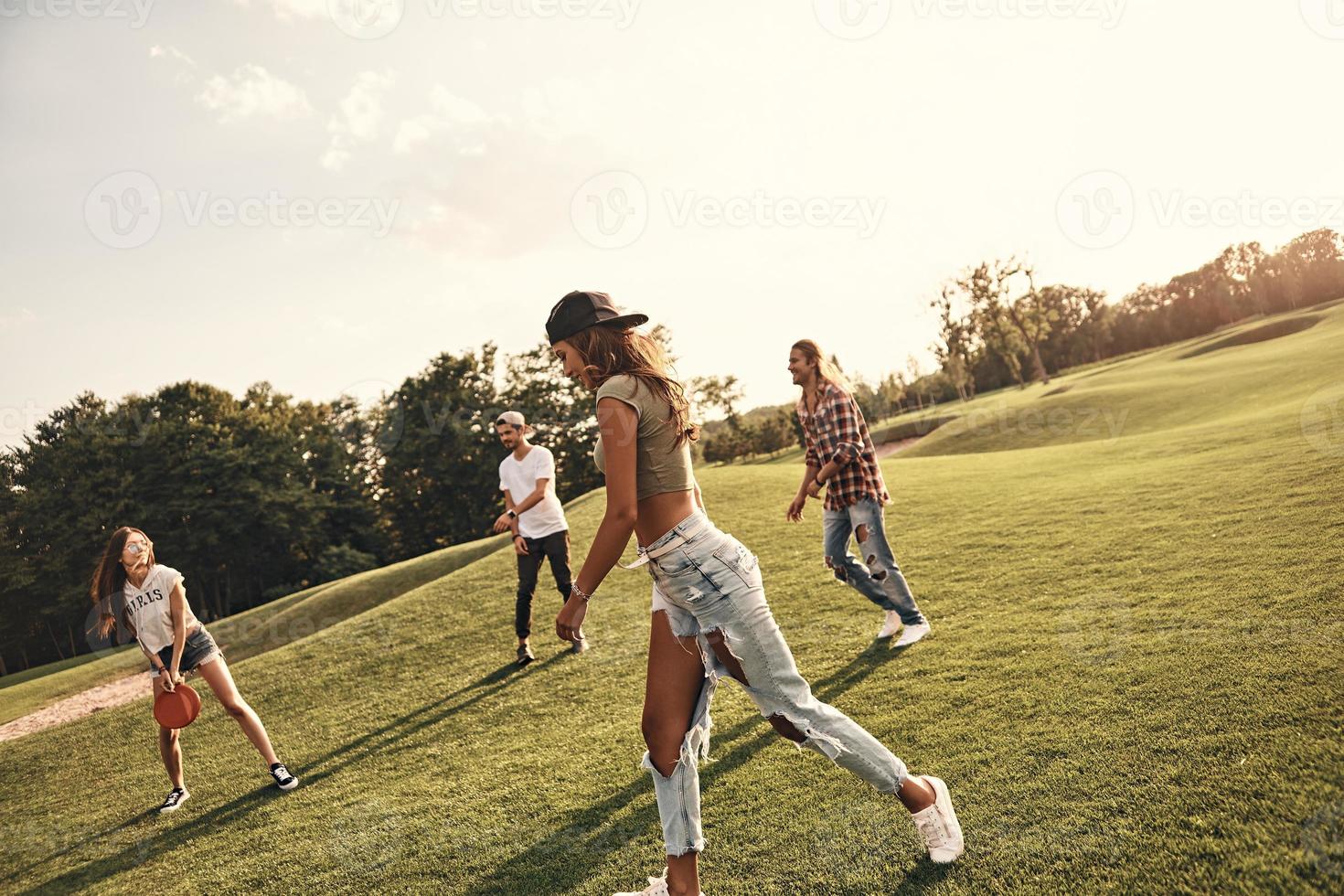 sommar aktivitet. grupp av ung människor i tillfällig ha på sig spelar frisbee medan utgifterna sorglös tid utomhus foto