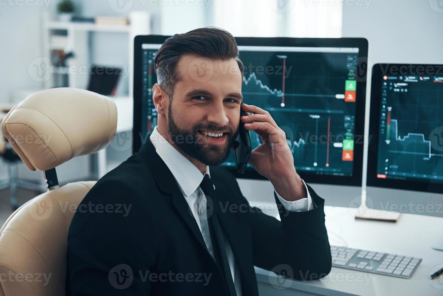 stilig ung man i skjorta och slips talande på de telefon och leende medan arbetssätt i de kontor foto