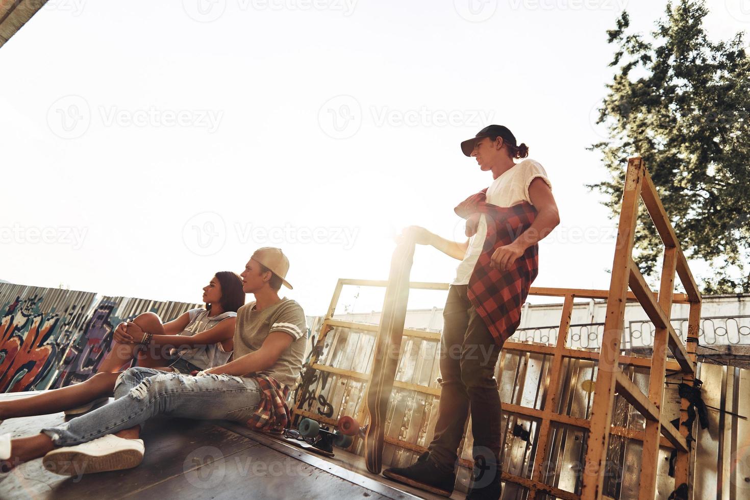 perfekt dag till skridsko. grupp av ung modern människor hängande ut tillsammans medan utgifterna tid på de skridsko parkera utomhus foto