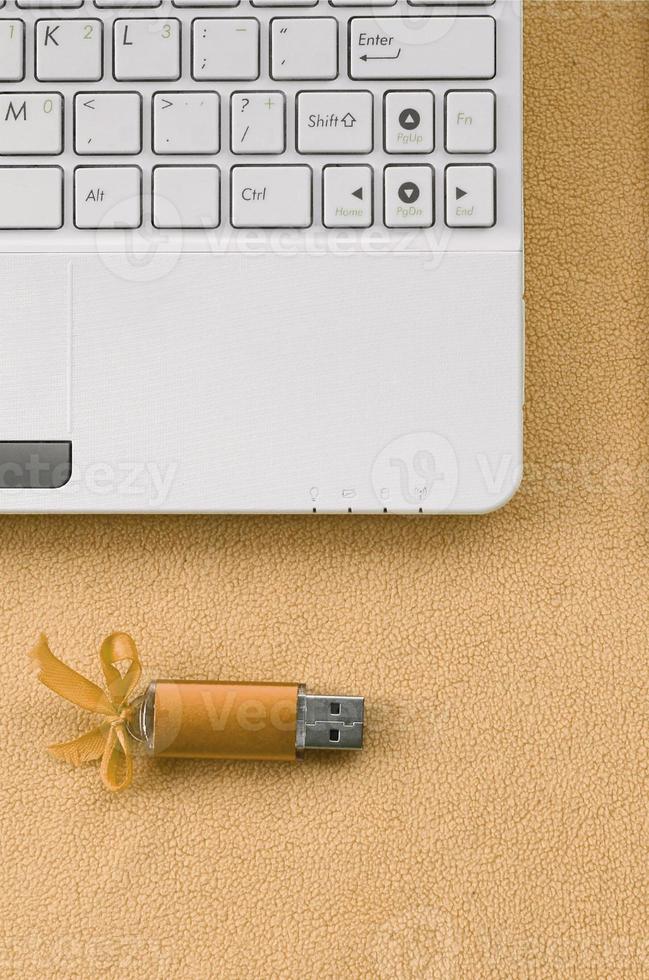 orange uSB blixt minne kort med en rosett lögner på en filt av mjuk och hårig ljus orange skinna tyg bredvid till en vit bärbar dator. klassisk kvinna gåva design för en minne kort foto