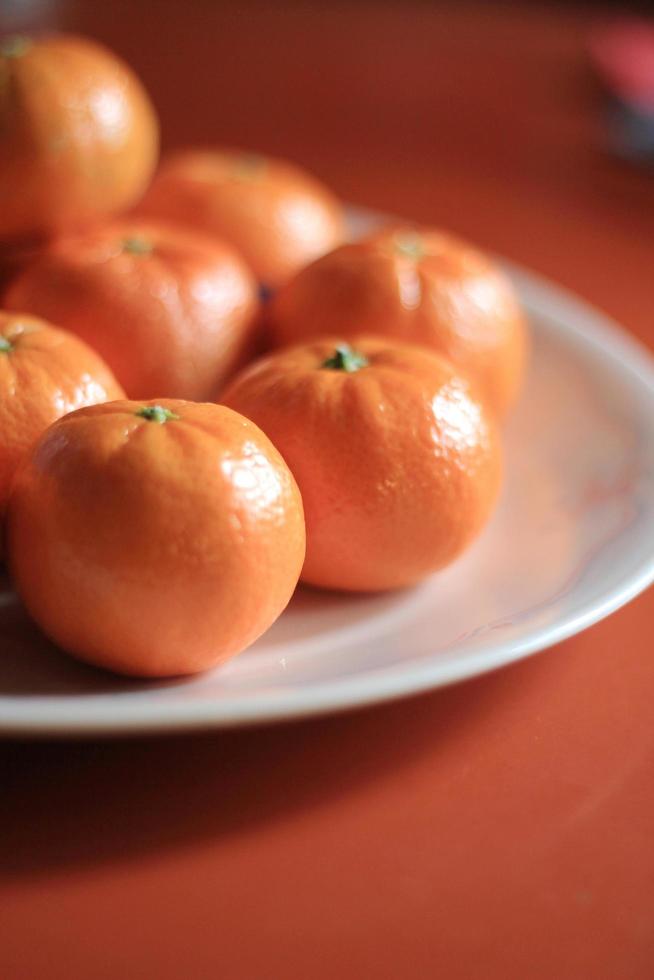 små apelsiner är placerad i en vit tallrik på de orange tabell. foto