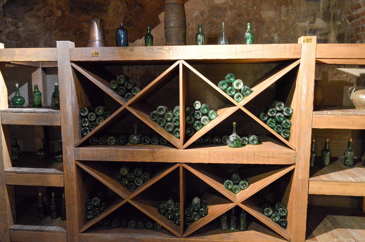 årgång grön tömma vin och öl glas flaskor i en vin skåp med hyllor i ett gammal medeltida murad sten källare foto
