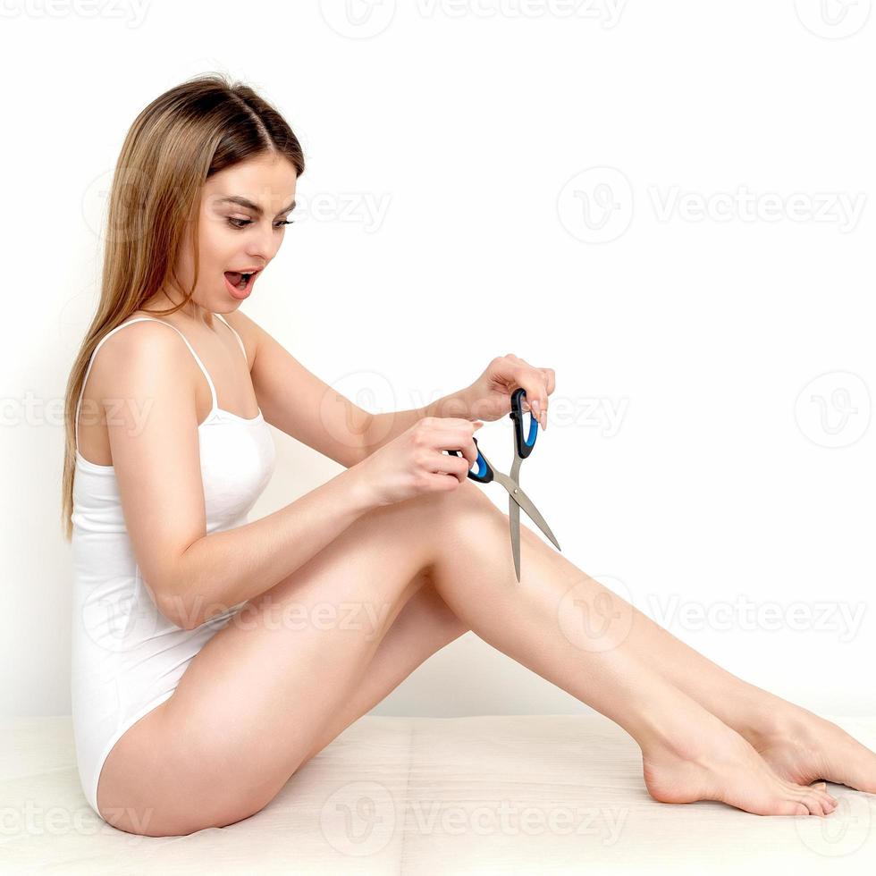 kvinna nedskärningar hår på henne ben förbi sax foto