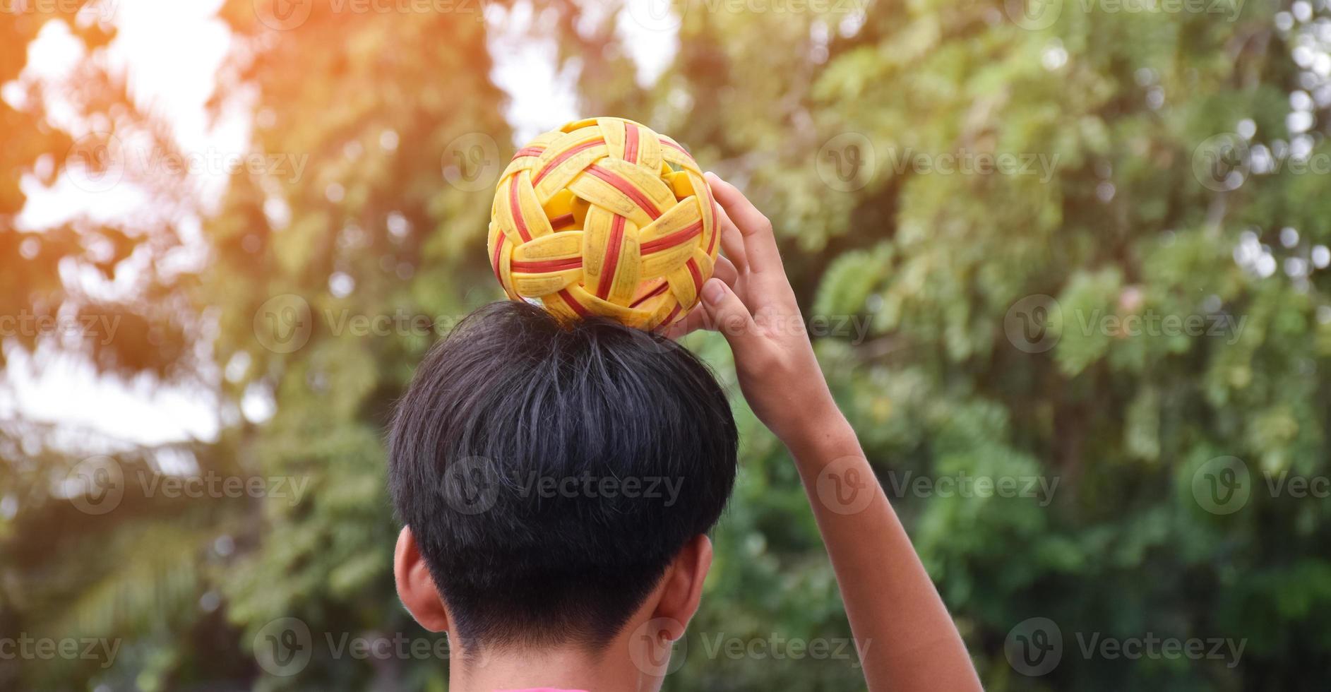 ung sydöst asiatisk manlig sepak takraw spelare använder sig av hans rätt hand till håll boll på hans huvud, utomhus- sepak takraw spelar efter skola, mjuk och selektiv fokus på boll. foto