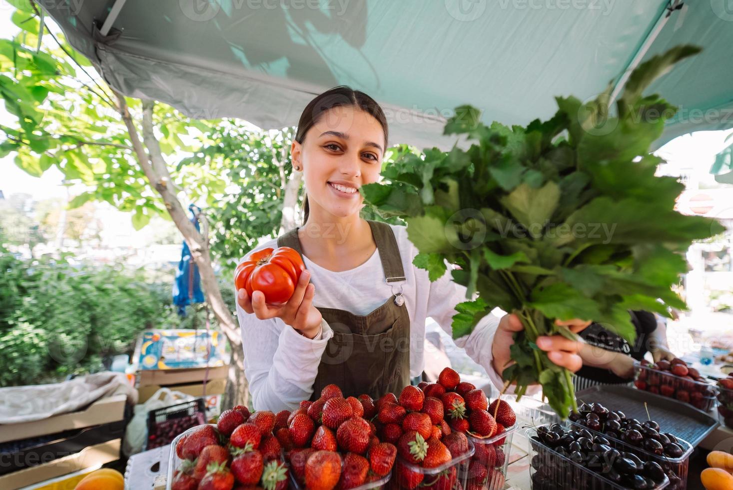 ung försäljare på arbete, innehav persilja och tomat i händer foto