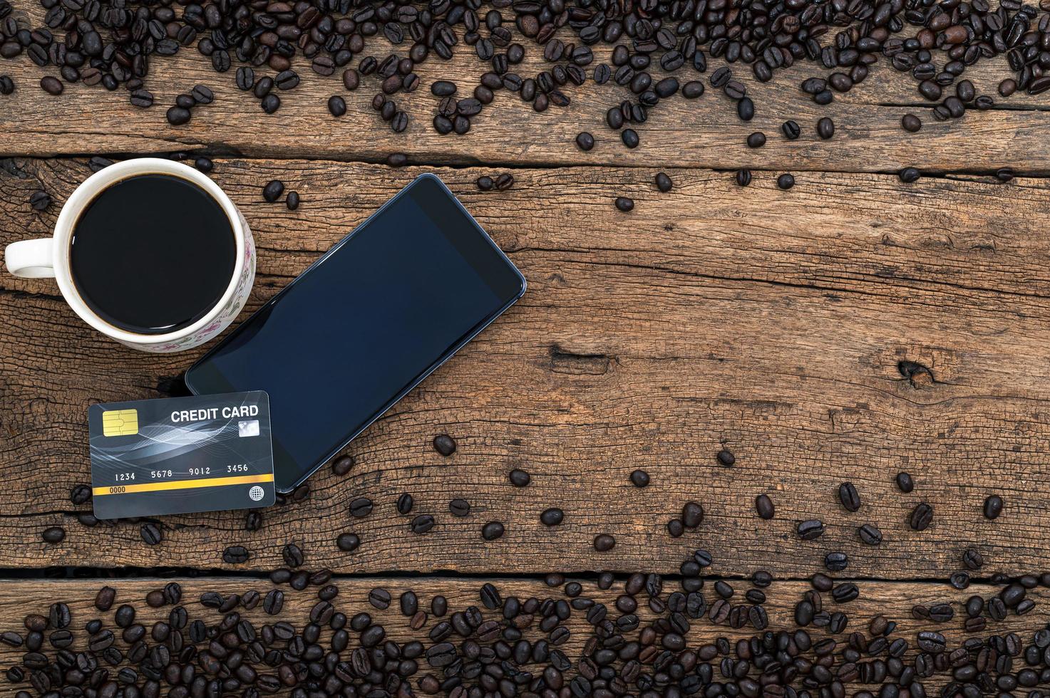 smartphone och ett kreditkort, en mugg kaffe och kaffebönor på skrivbordet foto
