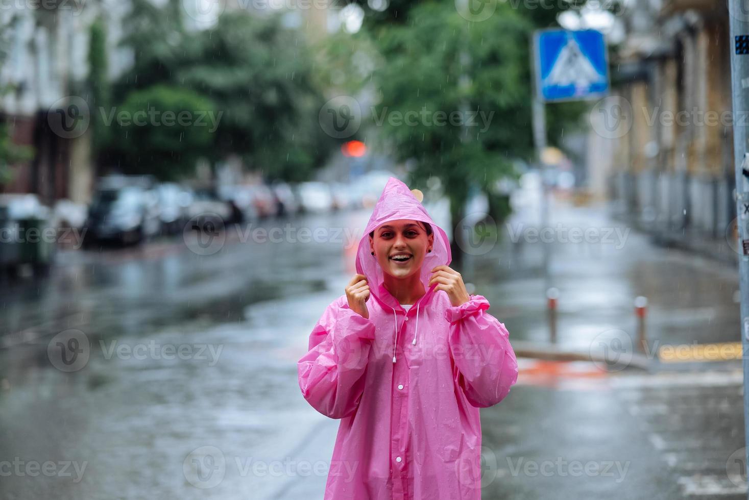 ung leende kvinna med regnkappa medan njuter en regnig dag. foto