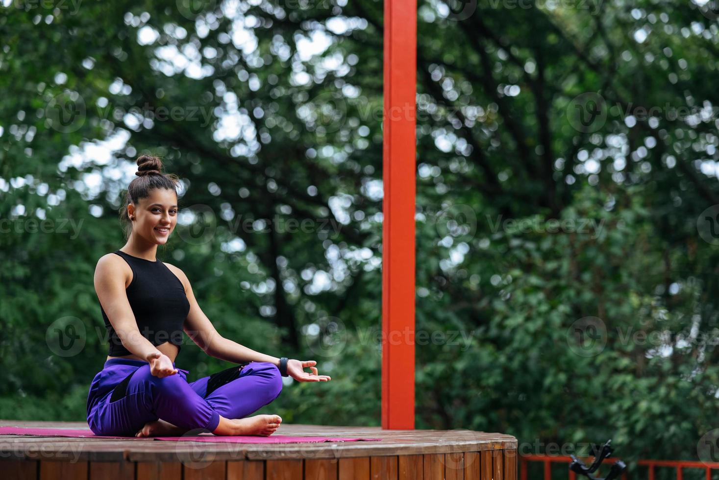 ung kvinna är praktiserande yoga Sammanträde i de lotus placera foto