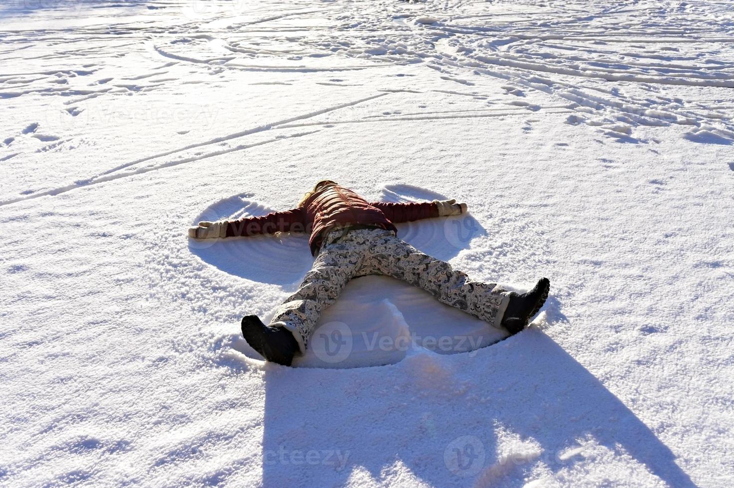 ung kvinna liggande i de snö och framställning en snö ängel. vinter- promenader och roligt foto