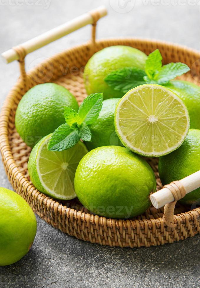 gröna limefrukter med färska myntablad på flätad bricka foto