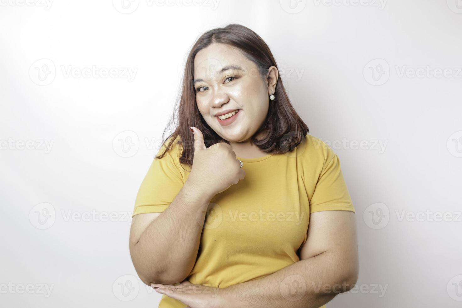 upphetsad asiatisk stor sized kvinna bär gul skjorta ger tummen upp hand gest av godkännande, isolerat förbi vit bakgrund foto