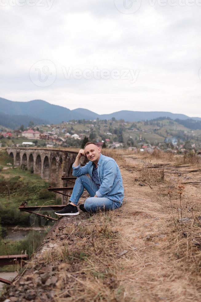 eleganta ung man på de järnväg bro i vorokhta, karpater mot de bakgrund av en berg landskap. turister Sammanträde i de bergen nära de järnväg foto