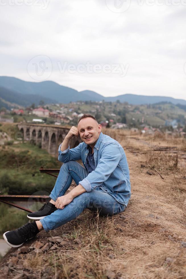 eleganta ung man på de järnväg bro i vorokhta, karpater mot de bakgrund av en berg landskap. turister Sammanträde i de bergen nära de järnväg foto