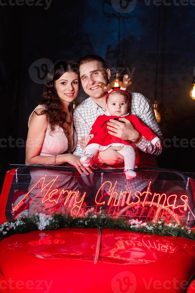 mamma, pappa och bebis flicka har roligt i de jul retro röd bil. föräldrar med en liten dotter i en jul Foto session. studio skytte innan de högtider.