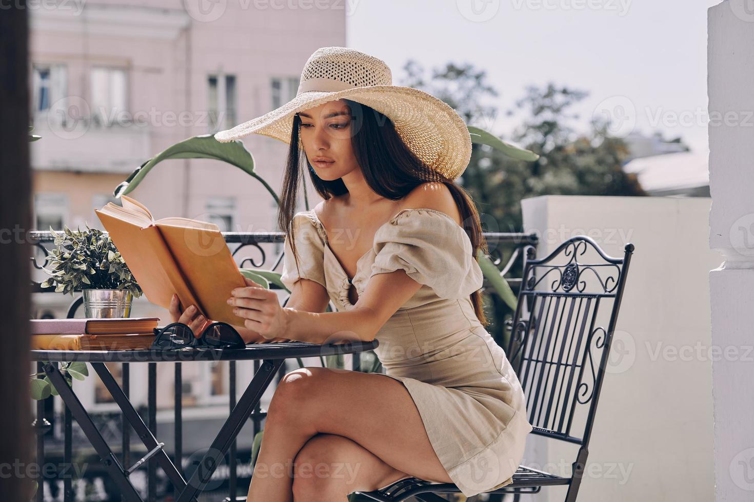 skön ung kvinna i elegant hatt läsning bok medan avkopplande på de balkong foto