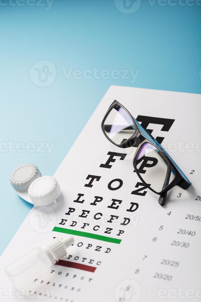 glasögon med Kontakt linser, droppar och ett optiker öga testa Diagram på en blå bakgrund. foto