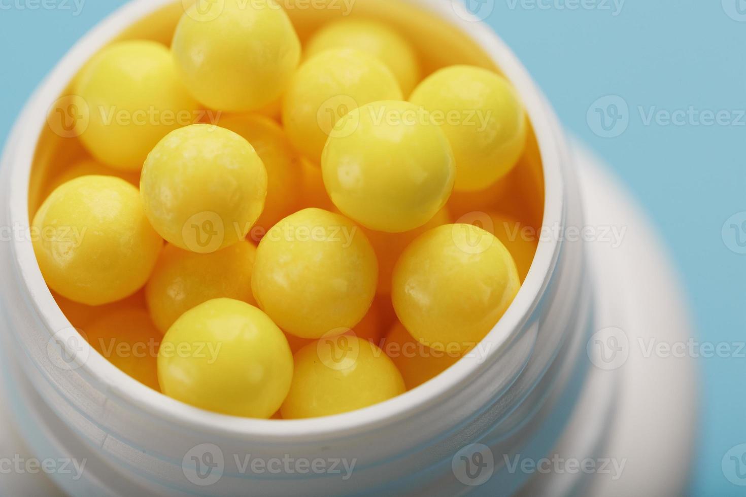 vitaminer av gul Färg i de form av runda dragéer i en vit burk på en blå bakgrund. foto