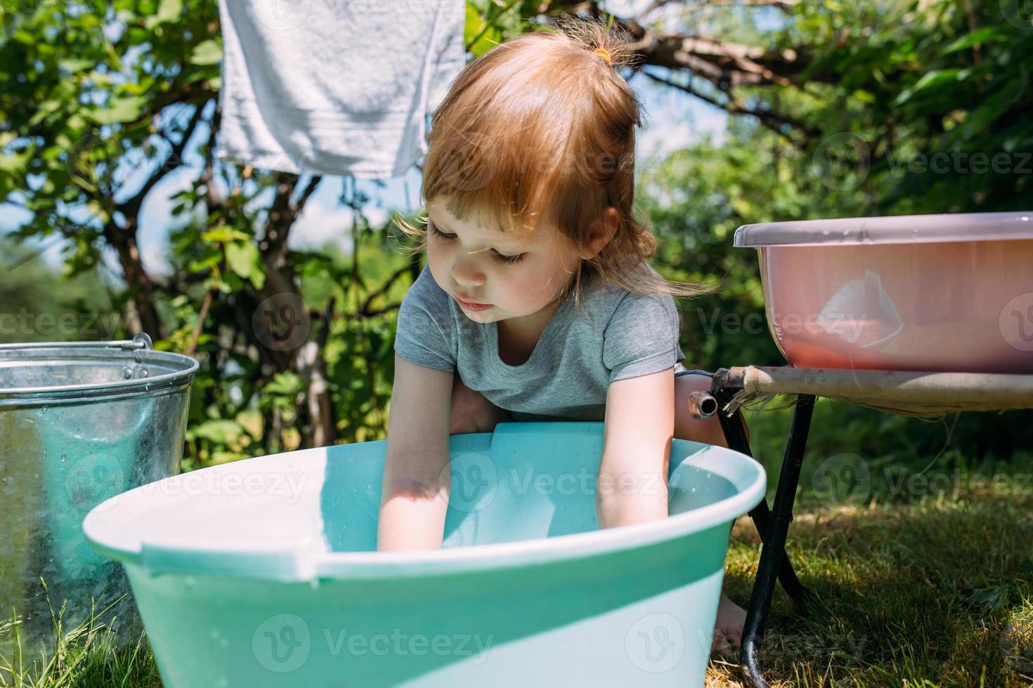 liten förskoletjej hjälper till med tvätten. barn tvättar kläder i trädgården foto