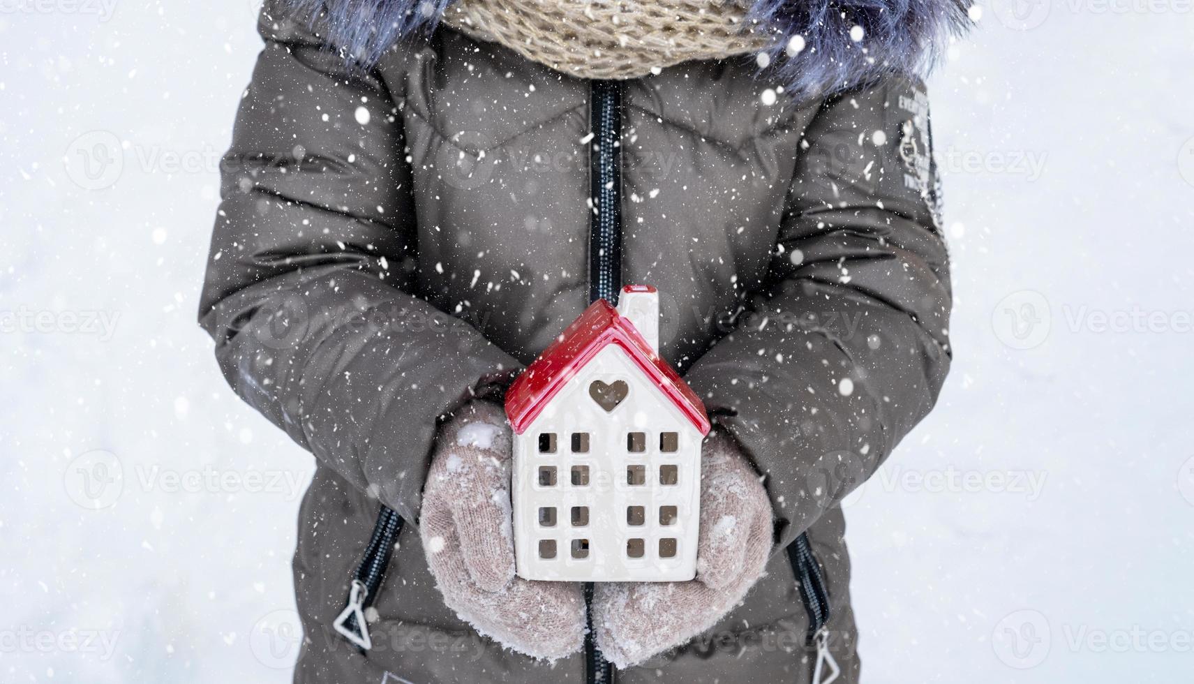hus, miniatyr- stuga i händer av flicka bär vantar och värma kläder utomhus- i snö. familj värden, inköp hus, flytt, inteckning. mysigt Hem, jul, ny år bokning foto