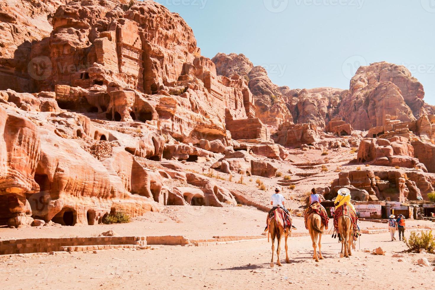 lokal- arab turist guide i petra stad ridning på kamel med turister följande grupp förbi kunglig petra gravar i solig varm dag foto