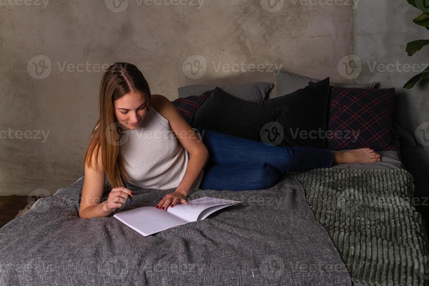 kvinna liggande på henne sida i säng och skrivning anteckningar i anteckningsbok foto