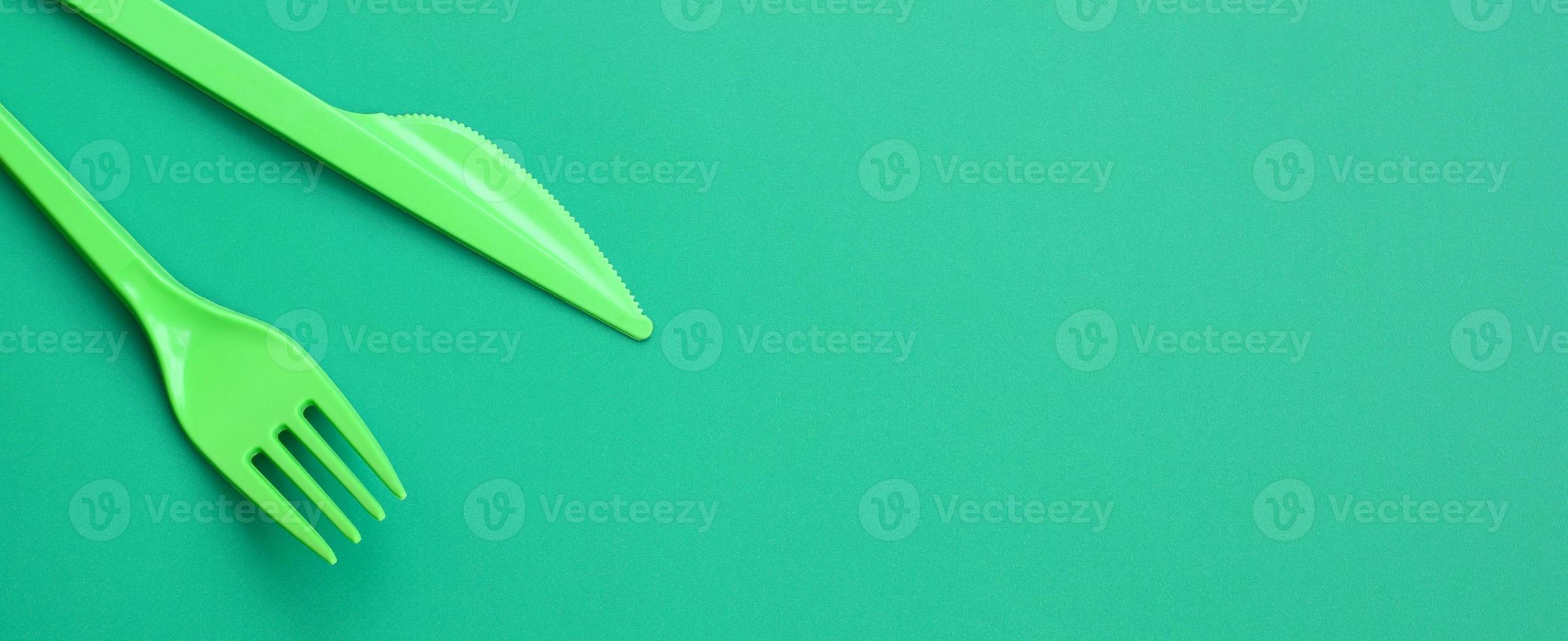 disponibel plast bestick grön. plast gaffel och kniv lögn på en grön bakgrund yta foto