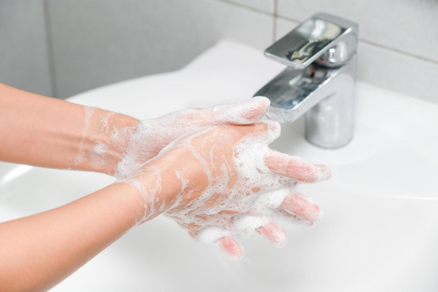kvinna använda sig av tvål och tvättning händer under de vatten knacka. foto