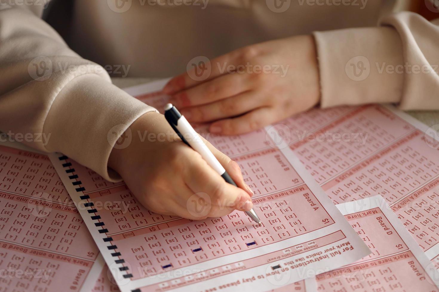fyllning ut en lotteri biljett. en ung kvinna spelar de lotteri och drömmar av vinnande de jackpott. kvinna hand märkning siffra på röd lotteri biljett foto