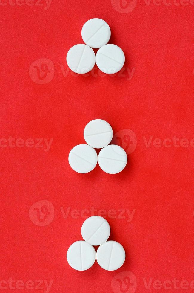 flera vit tabletter lögn på en ljus röd bakgrund i de form av tre triangel- pilar. bakgrund bild på medicin och farmaceutisk ämnen foto