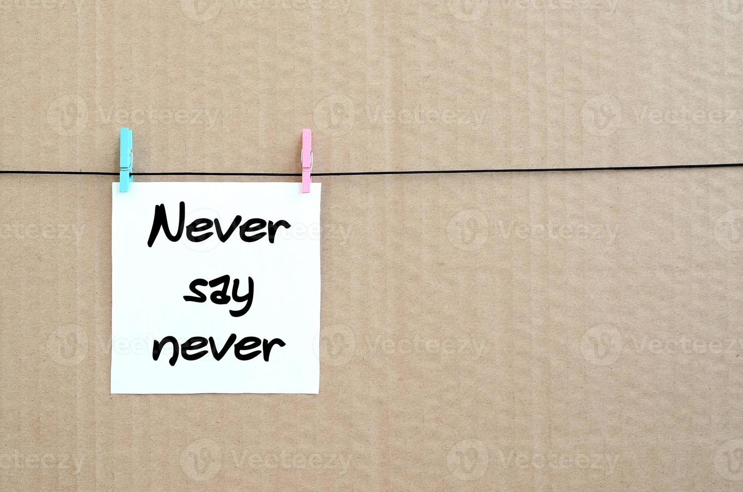 aldrig säga aldrig. notera är skriven på en vit klistermärke den där hänger med en klädnypa på en rep på en bakgrund av brun kartong foto