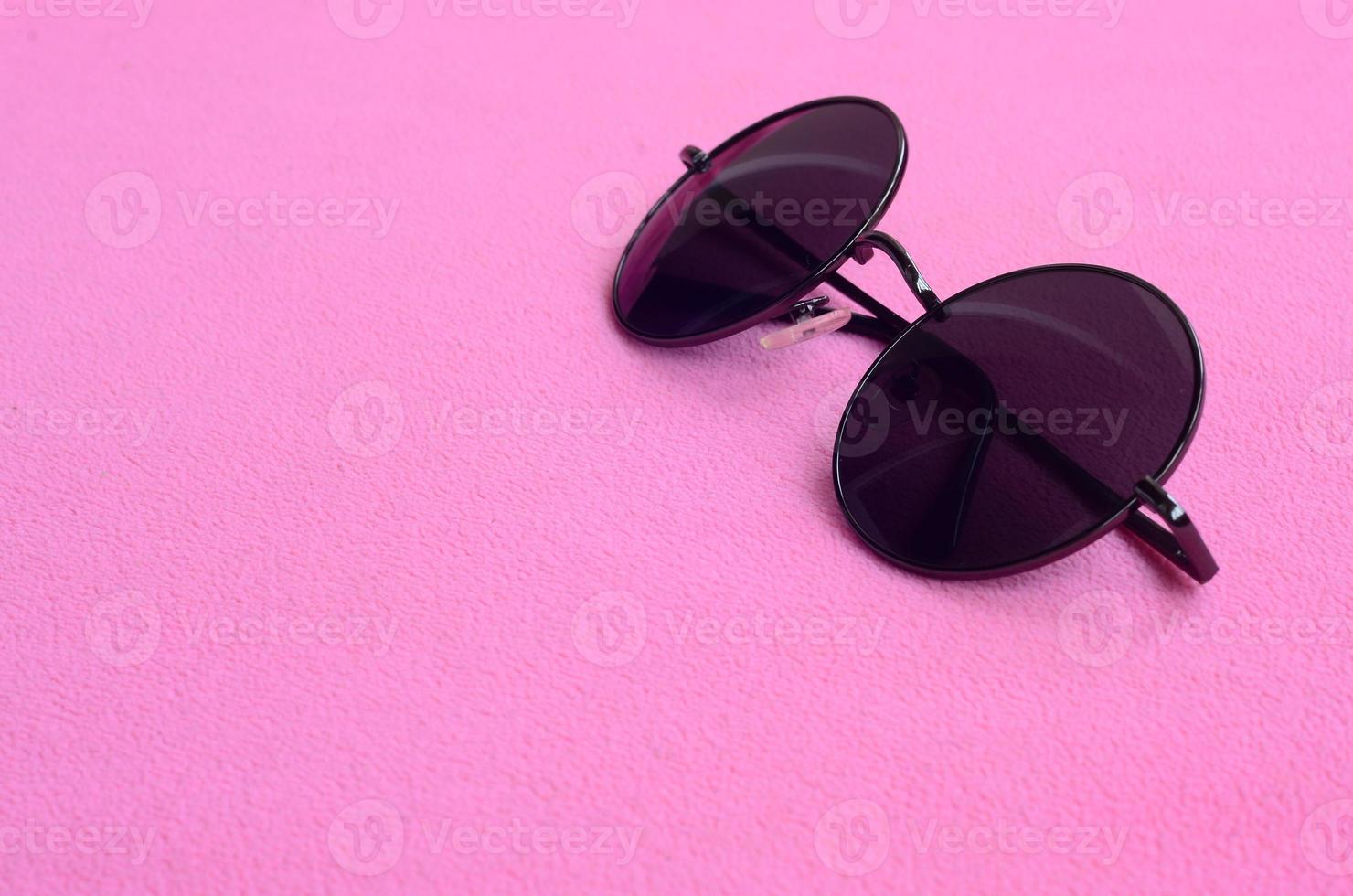 eleganta svart solglasögon med runda glasögon lögner på en filt tillverkad av mjuk och fluffig ljus rosa skinna tyg. modern bakgrund bild i kvinna färger foto