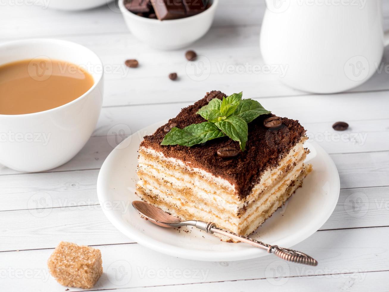 tiramisu efterrätt med mynta och kopp av kaffe på vit trä- tabell foto