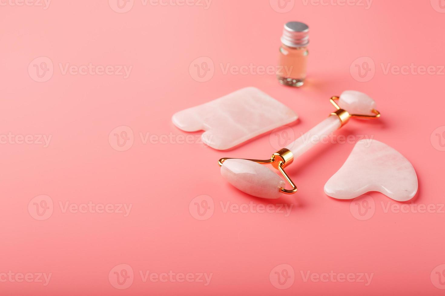 en uppsättning av verktyg för ansikte massage Metod gua sha tillverkad av naturlig reste sig kvarts på en rosa bakgrund. vält, jade sten och olja i en glas burk för ansikte och kropp vård. foto