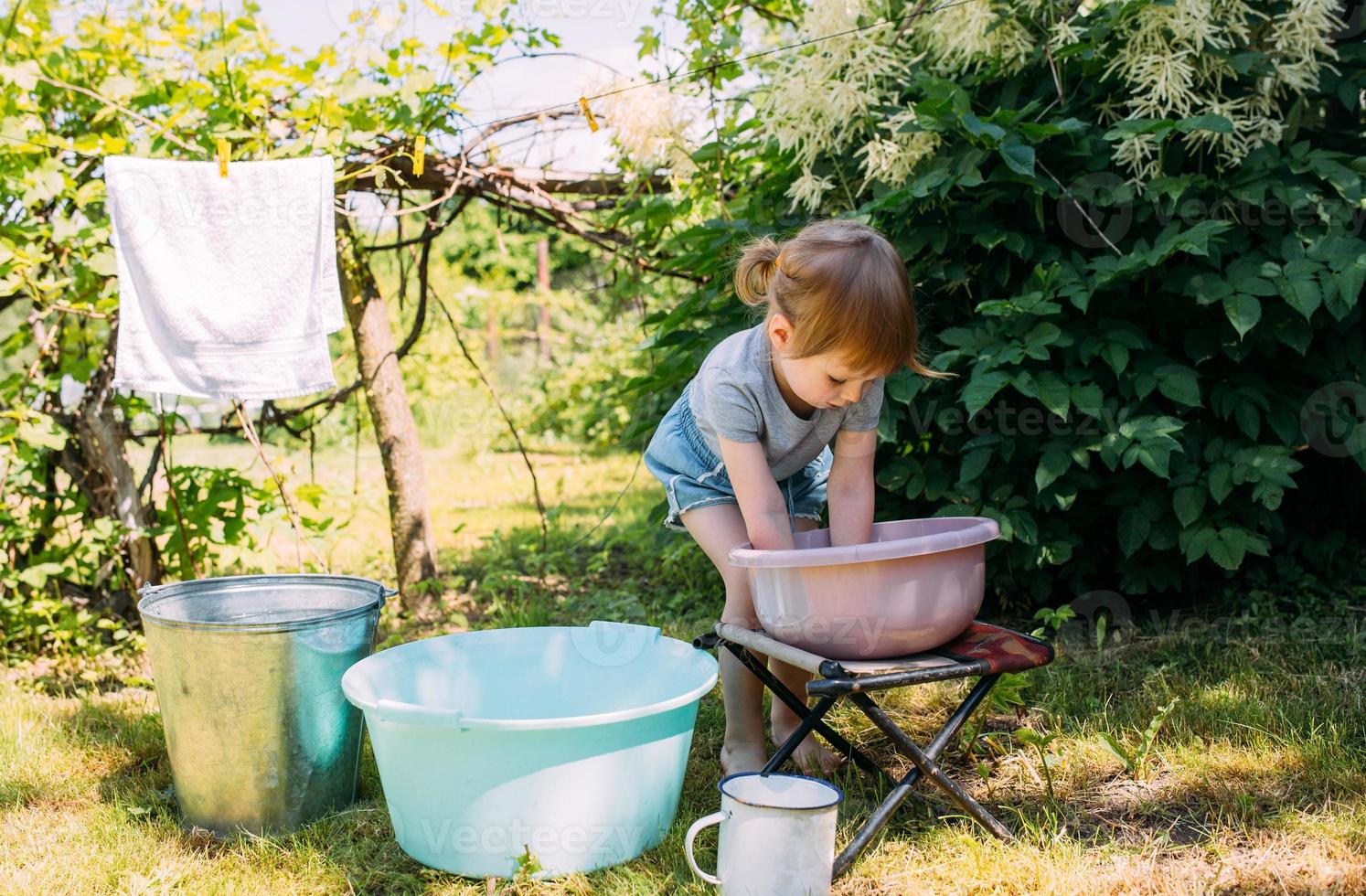 liten förskoletjej hjälper till med tvätten. barn tvättar kläder i trädgården foto