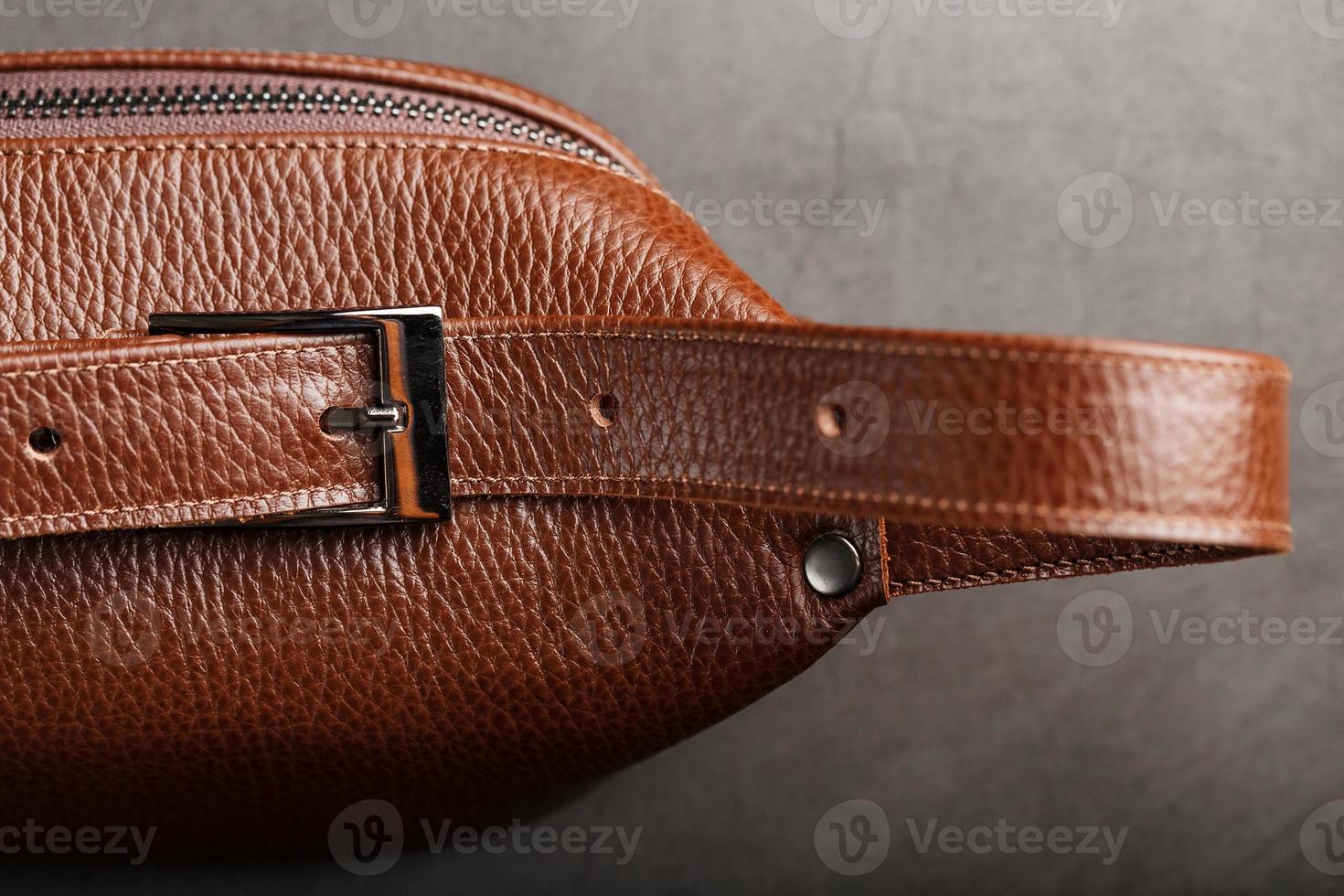 en brun bälte väska tillverkad av texturerad brun läder på en svart sten bakgrund. elegant Fanny packa brun väska med en dragkedja foto